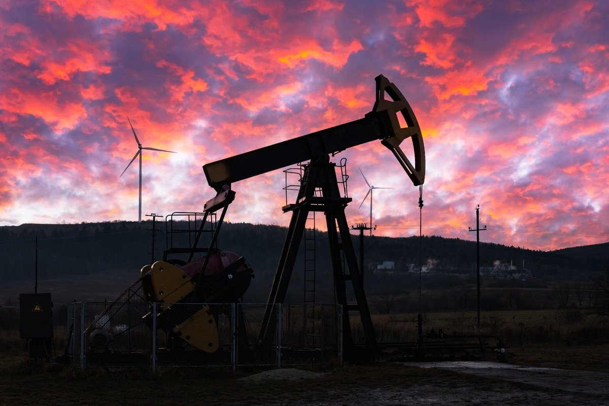 Oil pump jack silhouetted against a vivid red sunset on a hillside oilfield
