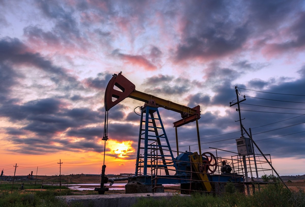 Oil pump jack beneath a dramatic purple dusk sky with workers at its base