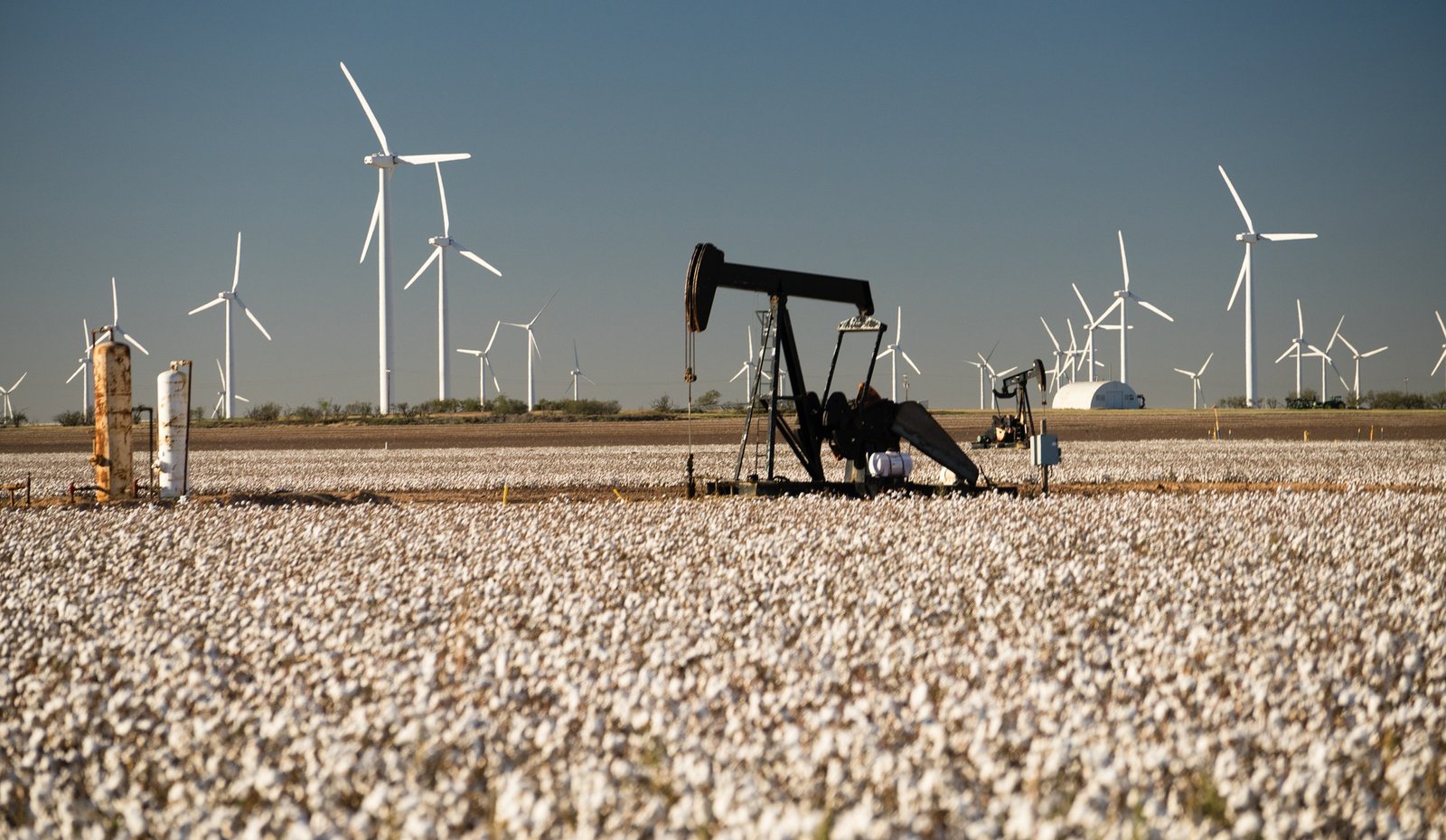 Oil pump jack with wind turbines on the horizon, contrasting traditional and renewable U.S. energy