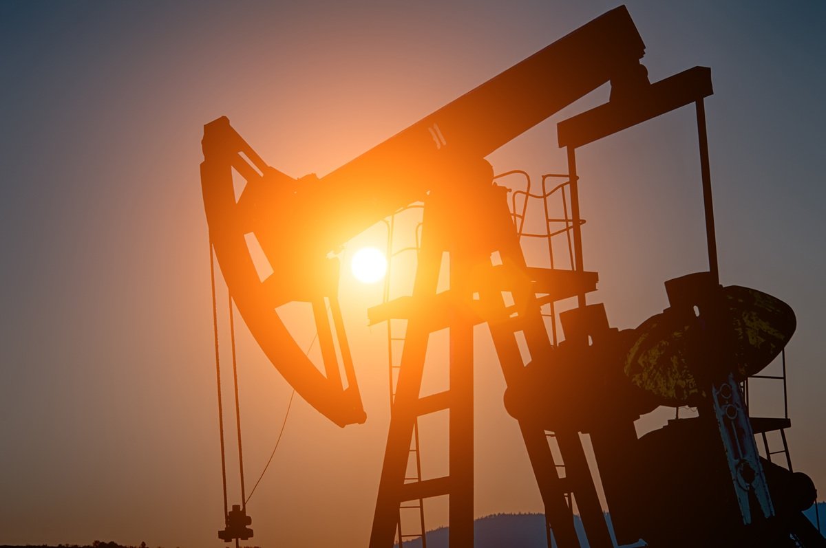 Oil pump jack silhouetted against a bright setting sun at a producing U.S. oil well