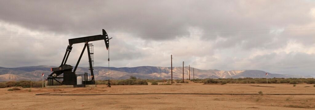 Lone oil pump jack standing in an open field under an overcast sky