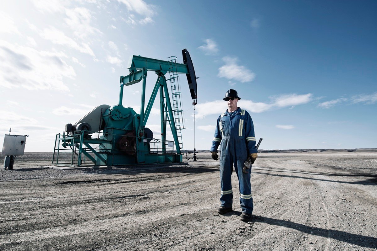 Oilfield worker in coveralls walking past a green pump jack in a U.S. desert oilfield